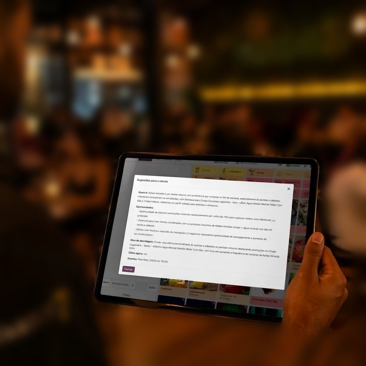 Tablet com o PDV do Valfredo sugerindo uma abordagem para o cliente, num salão cheio ao fundo